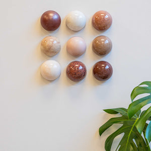Nine spherical ceramic domes on a light surface with a plant leaf in the corner